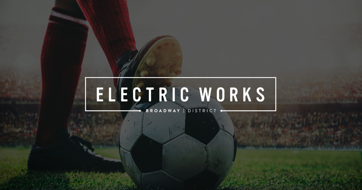 Soccer ball on the grass with a player's boot about to kick, overlaid by a white-framed “Electric Works” branding banner.